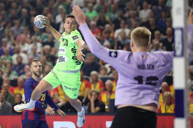 Fuechse Berlin's German left wing Tim Freihoefer (C) attempts to score past FC Barcelona's Danish goalkeeper #12 Emil Nielsen during the EHF Men's Handball Champions League Final 4 final between Barca and Fuechse Berlin in Cologne, western Germany on June 14, 2026. (Photo by Ronny HARTMANN / AFP)