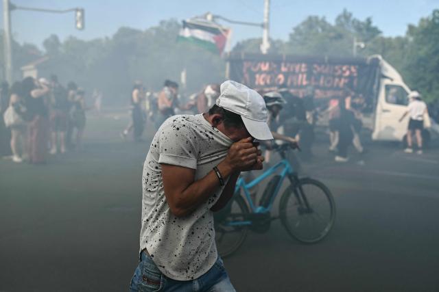 A demonstrator puts his face in his t-shirt as he reacts to tear gas during a rally of a "No-G7" coalition of over 60 associations, unions and left-wing groups "against fascism and imperialism, a day ahead of the summit's start, in Geneva on June 14, 2026. The 2026 edition of the G7 summit is set to take place June 15 to 17 in the French town of Evian-les-Bains near Switzerland, attended by country leaders as well as the EU's foreign policy chief and ministers from Brazil, Canada, the United Arab Emirates and Turkey. (Photo by Fabrice COFFRINI / AFP)