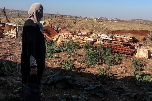 A Palestinian woman looks on from her home garden in the village of Beitin, northeast of Ramallah in the occupied West Bank, on June 14, 2026, as in the background are pictured a new Israeli outpost (front) and the Palestinian village of Taybeh (back). (Photo by Zain JAAFAR / AFP)