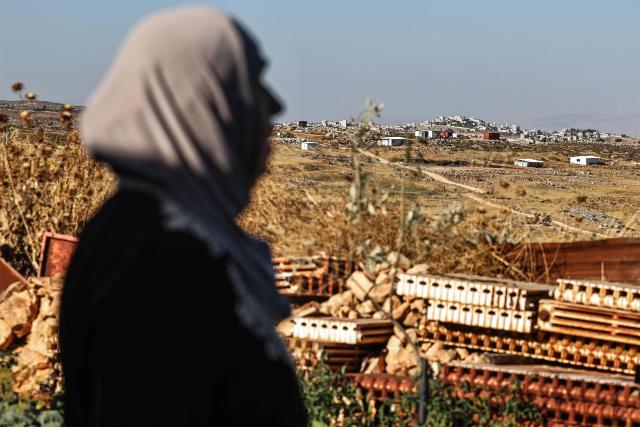 A Palestinian woman looks on from her home garden in the village of Beitin, northeast of Ramallah in the occupied West Bank, on June 14, 2026, as in the background are pictured a new Israeli outpost (front) and the Palestinian village of Taybeh (back). (Photo by Zain JAAFAR / AFP)