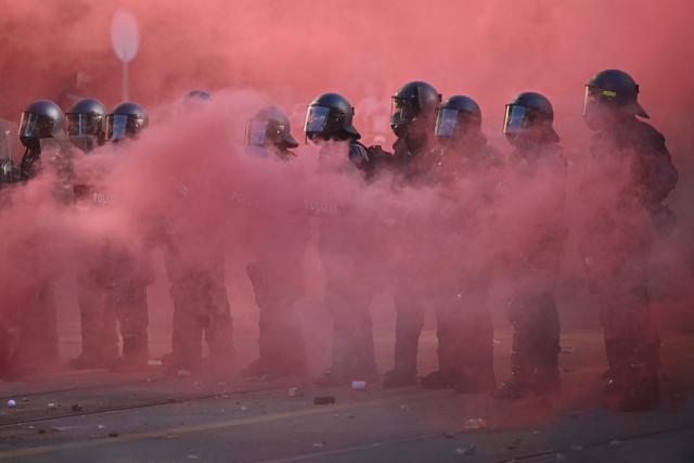 Police officers operate in riot gear with shields and rubber bullet guns amid a cloud of red smoke from a smoke bomb during a rally of a "No-G7" coalition of over 60 associations, unions and left-wing groups "against fascism and imperialism, a day ahead of the summit's start, in Geneva on June 14, 2026. The 2026 edition of the G7 summit is set to take place June 15 to 17 in the French town of Evian-les-Bains near Switzerland, attended by country leaders as well as the EU's foreign policy chief and ministers from Brazil, Canada, the United Arab Emirates and Turkey. (Photo by Fabrice COFFRINI / AFP)