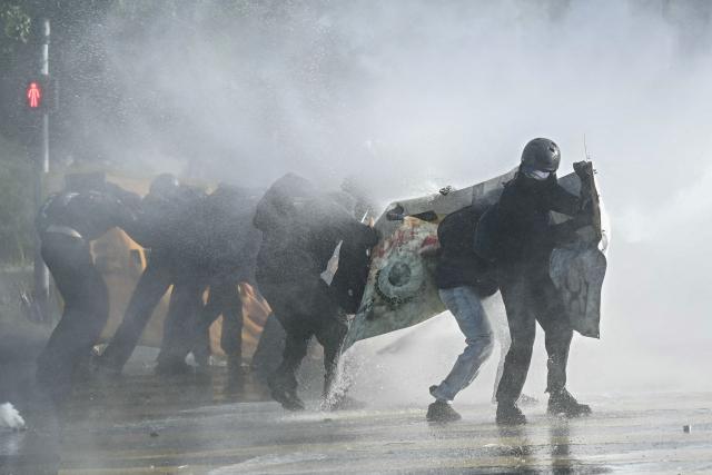 Demonstrators attempt to walk with a banner as they are hit by a police water cannon during a rally of a "No-G7" coalition of over 60 associations, unions and left-wing groups "against fascism and imperialism, a day ahead of the summit's start, in Geneva on June 14, 2026. The 2026 edition of the G7 summit is set to take place June 15 to 17 in the French town of Evian-les-Bains near Switzerland, attended by country leaders as well as the EU's foreign policy chief and ministers from Brazil, Canada, the United Arab Emirates and Turkey. (Photo by Fabrice COFFRINI / AFP)