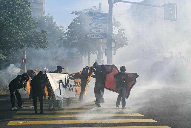 Demonstrators attempt to walk with a banner as they are hit by a police water cannon during a rally of a "No-G7" coalition of over 60 associations, unions and left-wing groups "against fascism and imperialism, a day ahead of the summit's start, in Geneva on June 14, 2026. The 2026 edition of the G7 summit is set to take place June 15 to 17 in the French town of Evian-les-Bains near Switzerland, attended by country leaders as well as the EU's foreign policy chief and ministers from Brazil, Canada, the United Arab Emirates and Turkey. (Photo by Fabrice COFFRINI / AFP)