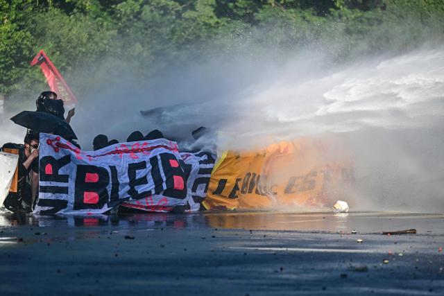 Demonstrators crouch with banners as they are hit by a police water cannon during a rally of a "No-G7" coalition of over 60 associations, unions and left-wing groups "against fascism and imperialism, a day ahead of the summit's start, in Geneva on June 14, 2026. The 2026 edition of the G7 summit is set to take place June 15 to 17 in the French town of Evian-les-Bains near Switzerland, attended by country leaders as well as the EU's foreign policy chief and ministers from Brazil, Canada, the United Arab Emirates and Turkey. (Photo by Fabrice COFFRINI / AFP)