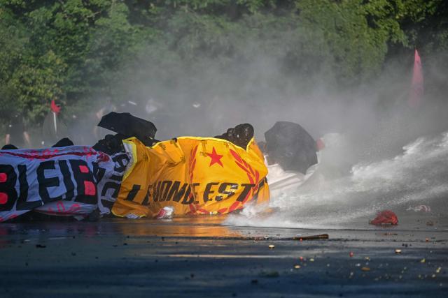 Demonstrators crouch with banners as they are hit by a police water cannon during a rally of a "No-G7" coalition of over 60 associations, unions and left-wing groups "against fascism and imperialism, a day ahead of the summit's start, in Geneva on June 14, 2026. The 2026 edition of the G7 summit is set to take place June 15 to 17 in the French town of Evian-les-Bains near Switzerland, attended by country leaders as well as the EU's foreign policy chief and ministers from Brazil, Canada, the United Arab Emirates and Turkey. (Photo by Fabrice COFFRINI / AFP)