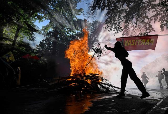 A demonstrator throws branches in the fire of a burning trash container during a rally of a "No-G7" coalition of over 60 associations, unions and left-wing groups "against fascism and imperialism, a day ahead of the summit's start, in Geneva on June 14, 2026. The 2026 edition of the G7 summit is set to take place June 15 to 17 in the French town of Evian-les-Bains near Switzerland, attended by country leaders as well as the EU's foreign policy chief and ministers from Brazil, Canada, the United Arab Emirates and Turkey. (Photo by Gabriel Monnet / AFP)