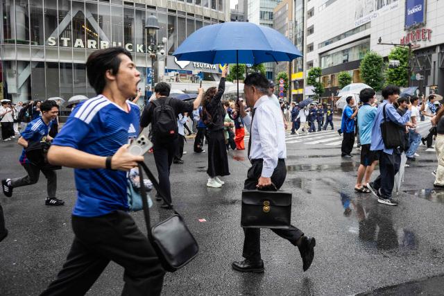 A man holds an umbrella as he goes to work while fans celebrate early in the morning at Shibuya Crossing in Tokyo, Japan, on June 15, 2026, after Japan’s 2–2 draw with the Netherlands in the World Cup. (Photo by Andrew CABALLERO-REYNOLDS / AFP)