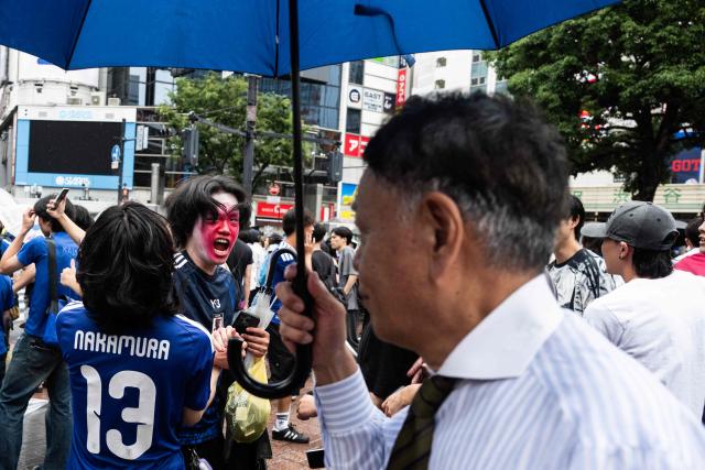 A man holds an umbrella as he goes to work while fans celebrate early in the morning at Shibuya Crossing in Tokyo, Japan, on June 15, 2026, after Japan’s 2–2 draw with the Netherlands in the World Cup. (Photo by Andrew CABALLERO-REYNOLDS / AFP)