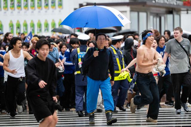 A man holds an umbrella on his way to work as fans celebrate early in the morning at Shibuya Crossing in Tokyo, Japan, on June 15, 2026, after Japan’s 2-2 draw with the Netherlands at the 2026 World Cup. (Photo by Andrew CABALLERO-REYNOLDS / AFP)