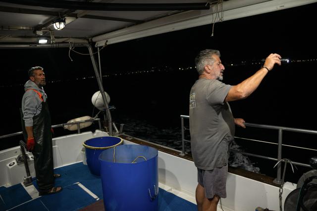 Fishermen Kostis Zevelekakis (L) and Michalis Zevelekakis (R) fish on their boat near the port of Ierapetra, on the island of Crete on June 3, 2026. Pufferfish, a warm-water invasive species, were first spotted in Greek waters some 20 years ago and are wreaking havoc with the country's fishing industry, a pillar of the nation's agricultural exports. The pufferfish explosion in Greek waters is the latest example of how warming oceans are changing ecosystems and upturning their reliant economies. (Photo by Angelos TZORTZINIS / AFP)