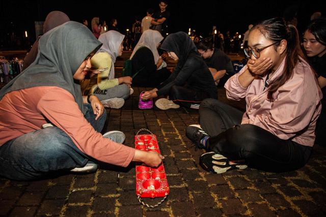 Members of the "Playing Community" group participate in congklak, an Indonesian children's game, at the Gelora Bung Karno Stadium compounds in Jakarta on May 22, 2026. Members of the group gather after work every Friday to let off steam by playing nostalgic Indonesian children's games. Similar get-togethers have sprung up elsewhere in the Southeast Asian nation as larger numbers of burnt-out workers seek novel solutions for handling stress and maintaining mental health. (Photo by Aditya Irawan / AFP) / To go with 'Indonesia-Social-Game-Psychology' Feature by Dessy SAGITA