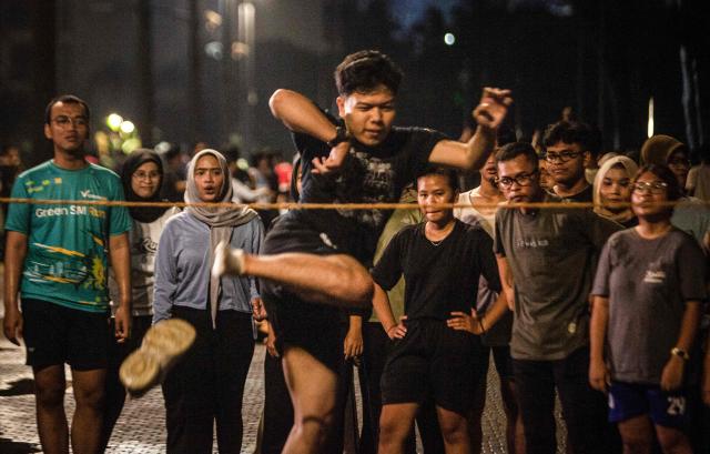 Members of the "Playing Community" look on as a another takes part in lompat tali karet (jump rope), an Indonesian children's game, at the Gelora Bung Karno Stadium compounds in Jakarta on May 22, 2026. Members of the group gather after work every Friday to let off steam by playing nostalgic Indonesian children's games. Similar get-togethers have sprung up elsewhere in the Southeast Asian nation as larger numbers of burnt-out workers seek novel solutions for handling stress and maintaining mental health. (Photo by Aditya Irawan / AFP) / To go with 'Indonesia-Social-Game-Psychology' Feature by Dessy SAGITA