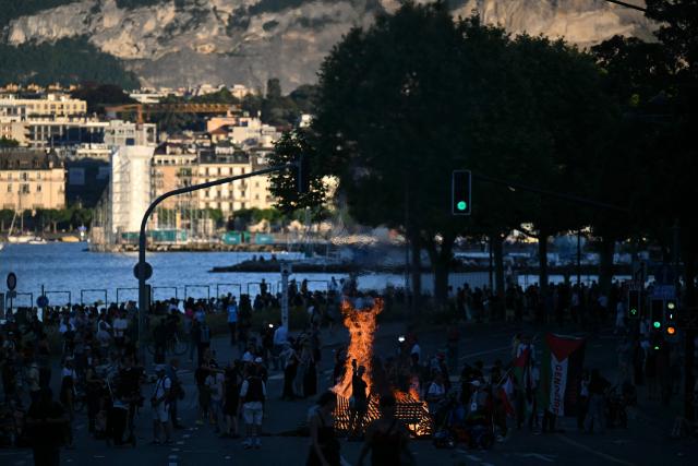 This photograph shows a fire burning in a street with the Lake Geneva in the background during a rally of a "No-G7" coalition of over 60 associations, unions and left-wing groups "against fascism and imperialism, a day ahead of the summit's start, in Geneva on June 14, 2026. The 2026 edition of the G7 summit is set to take place June 15 to 17 in the French town of Evian-les-Bains near Switzerland, attended by country leaders as well as the EU's foreign policy chief and ministers from Brazil, Canada, the United Arab Emirates and Turkey. (Photo by Fabrice COFFRINI / AFP)