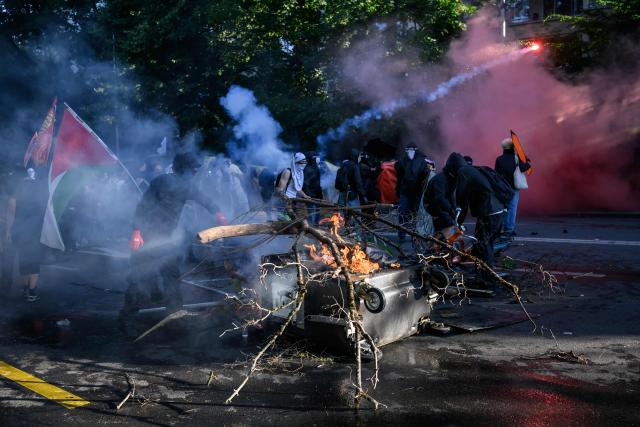 A demonstrator throws a branch in the fire of a burning trash container during a rally of a "No-G7" coalition of over 60 associations, unions and left-wing groups "against fascism and imperialism, a day ahead of the summit's start, in Geneva on June 14, 2026. The 2026 edition of the G7 summit is set to take place June 15 to 17 in the French town of Evian-les-Bains near Switzerland, attended by country leaders as well as the EU's foreign policy chief and ministers from Brazil, Canada, the United Arab Emirates and Turkey. (Photo by Fabrice COFFRINI / AFP)