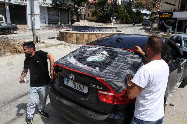 A resident displaced by the fighting places a banner depicting slain Hezbollah leader Hassan Nasrallah onto his car as he returns to Nabatieh on June 15, 2026. Israel's defence minister said on June 15, that Israeli forces would remain in Lebanon, Syria and Gaza indefinitely, hours after the United States and Iran agreed to end the Middle East war, including in Lebanon. (Photo by Mahmoud ZAYYAT / AFP) / 