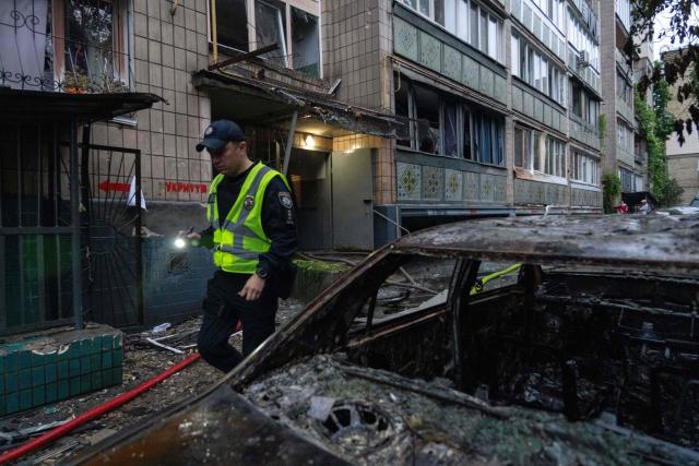A Police officer walks past a burnt down vehicle at the foot of a residential building, which was hit during a Russian missile and drone strike on the Ukrainian capital Kyiv on June 15, 2026, amid the Russian invasion of Ukraine. Russia fired a barrage of missiles at several major Ukrainian cities, setting fire to Kyiv's historic Dormition Cathedral at the UNESCO world heritage site Kyiv-Pechersk Lavra and killing eleven, while Ukraine strikes claimed three lives in a city south of Moscow. (Photo by OLEKSII FILIPPOV / AFP)
