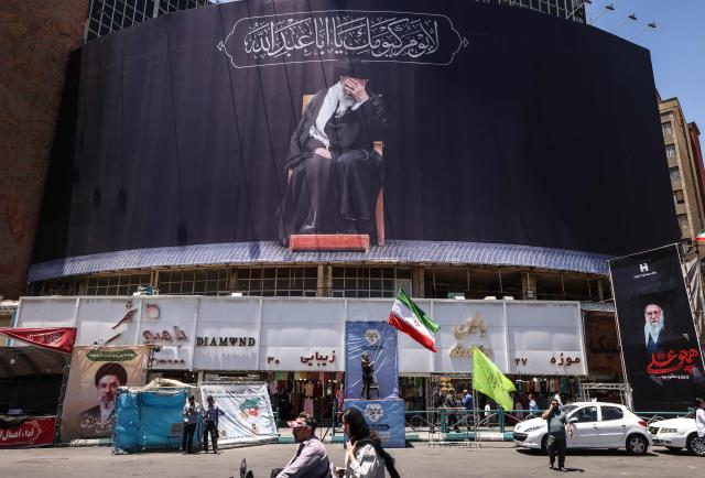 An Iranian woman waves a national flag under a billboard depicting slain supreme leader Ayatollah Ali Khamenei at Valiasr Square in Tehran on June 15, 2026. The United States and Iran agreed a peace deal and an "immediate and permanent" end to military operations on all fronts including Lebanon, mediator Pakistan said, signaling the apparent end to more than three months of war in Middle East. (Photo by ATTA KENARE / AFP) / 