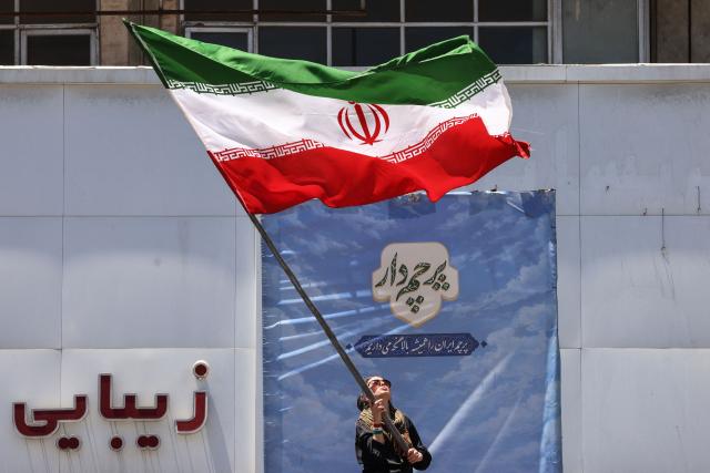 An Iranian woman waves a national flag at Valiasr Square in Tehran on June 15, 2026. The United States and Iran agreed a peace deal and an "immediate and permanent" end to military operations on all fronts including Lebanon, mediator Pakistan said, signaling the apparent end to more than three months of war in Middle East. (Photo by ATTA KENARE / AFP) / 
