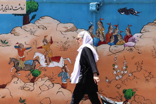 An Iranian woman walks past an epic mural depicting scenes from ancient and poetic stories in Tehran on June 15, 2026. The United States and Iran agreed a peace deal and an "immediate and permanent" end to military operations on all fronts including Lebanon, mediator Pakistan said, signaling the apparent end to more than three months of war in Middle East. (Photo by ATTA KENARE / AFP) / 