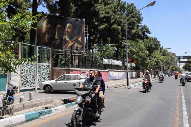 Iranians ride past a billboard depicting Iran's late supreme leader Ayatollah Ruhollah Khomeini (L), his successor, the late Ayatollah Ali Khamenei (C), and the new supreme leader Mojtaba Khamenei outside the former US embassy in Tehran on June 15, 2026. The United States and Iran agreed a peace deal and an "immediate and permanent" end to military operations on all fronts including Lebanon, mediator Pakistan said, signaling the apparent end to more than three months of war in Middle East. (Photo by ATTA KENARE / AFP) / 