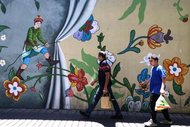 Iranians walk past a mural in Tehran on June 15, 2026. The United States and Iran agreed a peace deal and an "immediate and permanent" end to military operations on all fronts including Lebanon, mediator Pakistan said, signaling the apparent end to more than three months of war in Middle East. (Photo by ATTA KENARE / AFP) / 