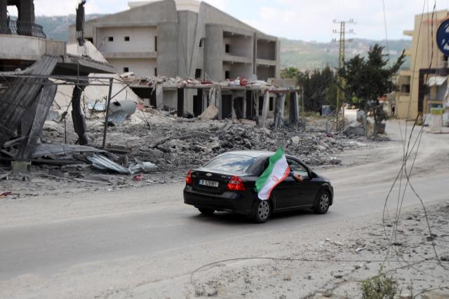 An Iranian national flag flutters from the widnow of a car as it drives through the southern Lebanese village of Siddqin, destroyed by Israeli military bombardment on June 15, 2026. Lebanon's army on June 15, urged displaced residents to delay their return to southern border villages, hours after an agreement was announced between Washington and Tehran to end the Middle East war, including in Lebanon. (Photo by Kawnat HAJU / AFP) / 