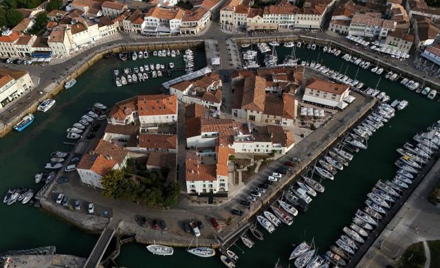This aerial photograph shows boats moored at a marina surrounding a little island in Saint-Martin-de-Ré, on the northern shore of the Ré island along the Atlantic Ocean, southwestern France on June 13, 2026. The marina consists in a circular tidal basin (R) protected by a lock (bottom) and shelters up to 280 boats. (Photo by Christophe ARCHAMBAULT / AFP)