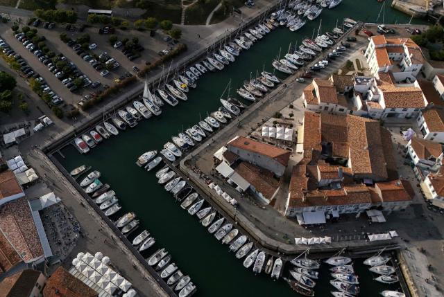This aerial photograph shows boats moored at a marina surrounding a little island in Saint-Martin-de-Ré, on the northern shore of the Ré island along the Atlantic Ocean, southwestern France on June 13, 2026. The marina consists in a circular tidal basin (R) protected by a lock (bottom) and shelters up to 280 boats. (Photo by Christophe ARCHAMBAULT / AFP)