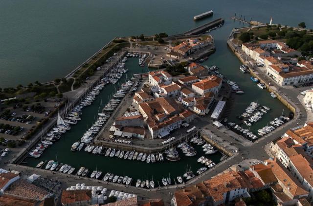 This aerial photograph shows boats moored at a marina surrounding a little island in Saint-Martin-de-Ré, on the northern shore of the Ré island along the Atlantic Ocean, southwestern France on June 13, 2026. The marina consists in a circular tidal basin (R) protected by a lock (bottom) and shelters up to 280 boats. (Photo by Christophe ARCHAMBAULT / AFP)