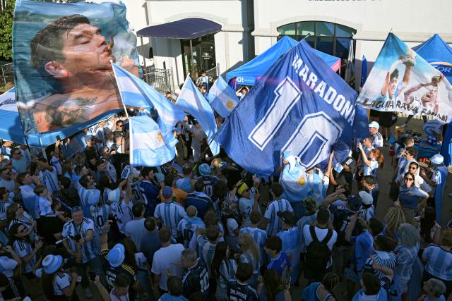 Argentina supporters Diego Maradona-themed flags as they take part in a "banderazo" flag-waving gathering outside "Los Hornos" restaurant that caters Argentinian barbecue specialties, near Kansas City, Missouri, United States on June 14, 2026, ahead of the 2026 World Cup football match between Argentina and Algeria. (Photo by JUAN MABROMATA / AFP)