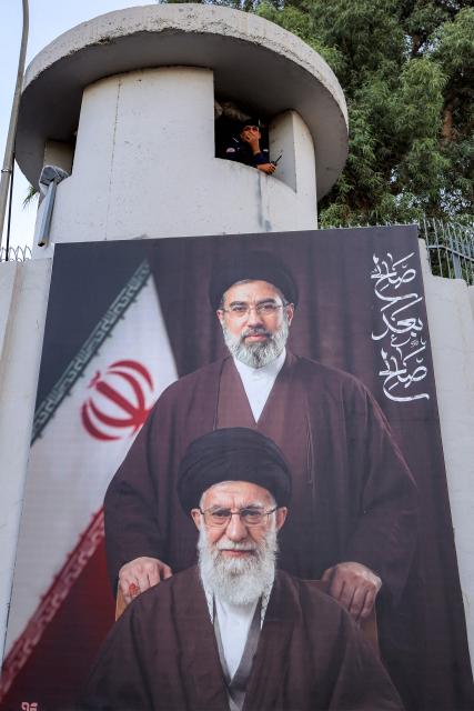 A member of the Iraqi security forces mans a watchtower displaying a giant artistic rendition of Iran's supreme leader Mojtaba Khamenei and his late father Ali Khamenei, outside the Iranian embassy headquarters in Baghdad on June 15, 2026, during celebrations following the announcement of a deal to end the war between Iran and the US. The US president said on June 15 that the Strait of Hormuz would be fully open later in the week, after Washington and Tehran announced a deal to end the Middle East war. Iran had blockaded the vital waterway since the start of the conflict after US-Israeli strikes on the Islamic republic in late February. (Photo by AHMAD AL-RUBAYE / AFP) / 