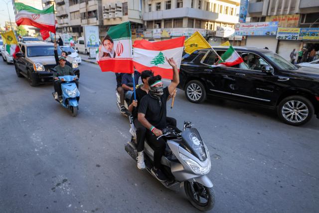 Youths ride scooters and vehicles while waving flags of Iraq, Iran, Lebanon and Hezbollah in Baghdad on June 15, 2026, during celebrations following the announcement of a deal to end the war between Iran and the US. The US president said on June 15 that the Strait of Hormuz would be fully open later in the week, after Washington and Tehran announced a deal to end the Middle East war. Iran had blockaded the vital waterway since the start of the conflict after US-Israeli strikes on the Islamic republic in late February. (Photo by AHMAD AL-RUBAYE / AFP) / 