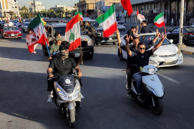 Youths ride scooters and vehicles while waving flags of Iraq, Iran, Lebanon and Hezbollah in Baghdad on June 15, 2026, during celebrations following the announcement of a deal to end the war between Iran and the US. The US president said on June 15 that the Strait of Hormuz would be fully open later in the week, after Washington and Tehran announced a deal to end the Middle East war. Iran had blockaded the vital waterway since the start of the conflict after US-Israeli strikes on the Islamic republic in late February. (Photo by AHMAD AL-RUBAYE / AFP) / 