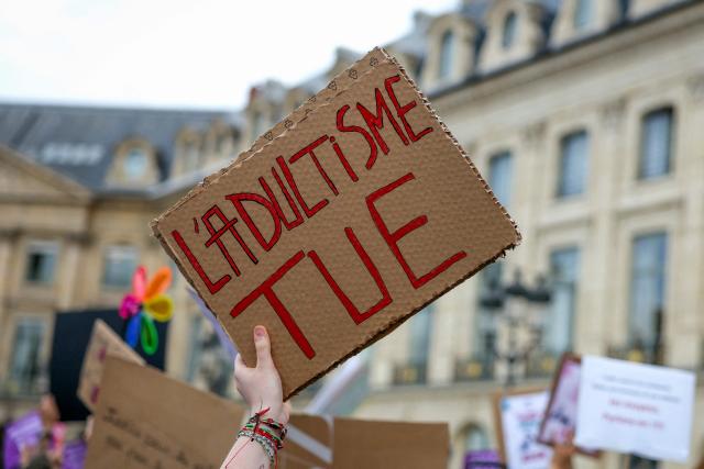 A protestor holds a slogan reading "Adultism kills" during a gathering to demand a law against violence on minors, outside the French Justice Ministry, in Place Vendome, in Paris on June 15, 2026. (Photo by Thomas SAMSON / AFP)