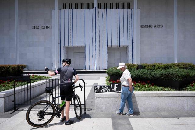 People stand in front of a tarp covering signage on the facade of the Kennedy Center in Washington, DC, on June 15, 2026, after a judge ordered the removal of US President Donald Trump's name from the building. Workers removed President Donald Trump's name from the facade of the prestigious Kennedy Center in Washington on June 13 -- a stinging defeat for the US leader who has eschewed political tradition to affix his name and likeness across public spaces. (Photo by Brendan Smialowski / AFP)