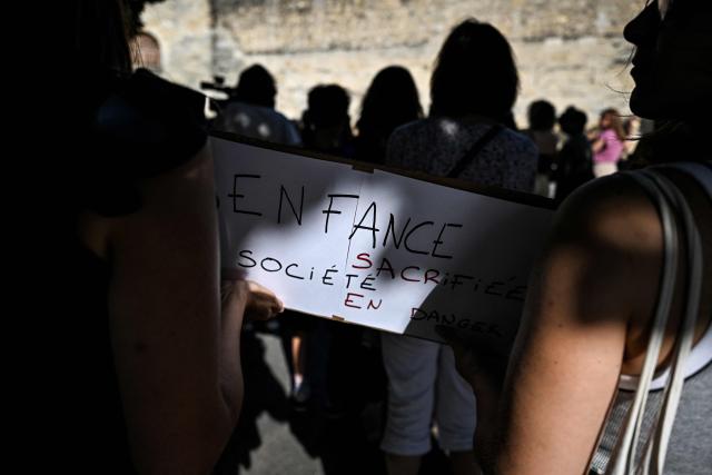 Protesters hold a sign reading "Sacrified childhood - society at risk" during a gathering to demand a law against violence on minors outside the Judicial court in Bordeaux, southwestern France on June 15, 2026. (Photo by Christophe ARCHAMBAULT / AFP)