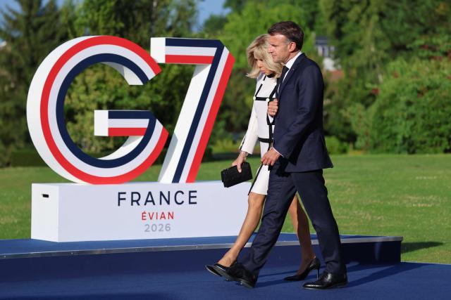 France's President Emmanuel Macron (R) and his wife Brigitte Macron walk past the G7 logo during the official greeting as part of the G7 summit, in Evian, eastern France, on June 15, 2026. A G7 summit is set to take place June 15 to 17 in the French town of Evian-les-Bains near Switzerland and it will be attended by country leaders as well as the EU's foreign policy chief and ministers from Brazil, Canada, the United Arab Emirates and Turkey. (Photo by Ludovic MARIN / AFP)