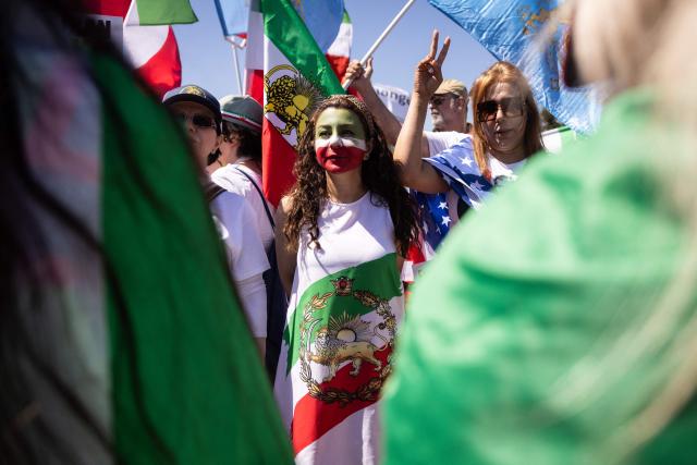 A woman wears an image of a pre-revolutionary Iranian flag as people gather to protest against the Iranian regime outside Los Angeles Stadium (SoFi Stadium) ahead of the 2026 World Cup football tournament match between Iran and New Zealand in Inglewood, California, on June 15, 2026. Hundreds of anti-regime protesters gathered outside the stadium in Los Angeles Monday where Iran will take on New Zealand in their opening game of the 2026 World Cup. (Photo by ETIENNE LAURENT / AFP)