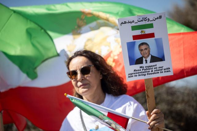 A woman holds a sign with a portrait of the son of the last shah of Iran,  Reza Pahlavi, as people protest against the Iranian regime outside Los Angeles Stadium (SoFi Stadium) ahead of the 2026 World Cup football tournament match between Iran and New Zealand in Inglewood, California, on June 15, 2026. Hundreds of anti-regime protesters gathered outside the stadium in Los Angeles Monday where Iran will take on New Zealand in their opening game of the 2026 World Cup. (Photo by ETIENNE LAURENT / AFP)