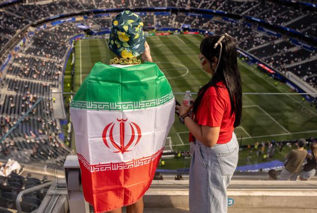 An Iranian fan wrapped in a national flag awaits the start of the 2026 World Cup Group G football match between Iran and New Zealand at Los Angeles Stadium in Inglewood on June 15, 2026.  (Photo by ETIENNE LAURENT / AFP)