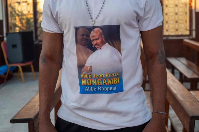 A young man wearing a t-shirt bearing the image of Father Jean-Pierre Mongambi attends a religious music event at the Bienheureuse Anuarite parish in Kinshasa on May 17, 2026. Jean-Pierre Mongambi, also known as “the rapping priest,” roams the most deprived neighbourhoods of the Congolese capital to evangelise young people.
He has become a celebrity in the DRC, and beyond, with rap tracks that reprise psalms and prayers, and concerts widely shared on social media. (Photo by Hardy BOPE / AFP)