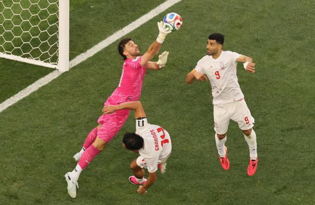 New Zealand's goalkeeper #01 Max Crocombe clears the ball past Iran's midfielder #14 Saman Ghoddos and forward #09 Mehdi Taremi during the 2026 World Cup Group G football match between Iran and New Zealand at Los Angeles Stadium in Inglewood on June 15, 2026.  (Photo by Etienne Laurent / AFP)