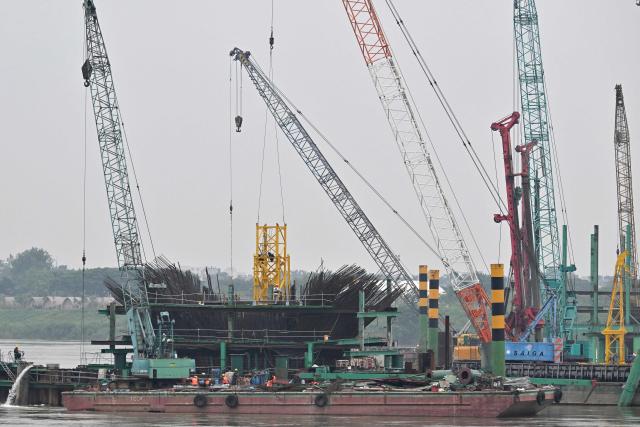 Workers use heavy construction equipment to build a new bridge over the Red River in Hanoi on June 16, 2026. (Photo by Nhac NGUYEN / AFP)