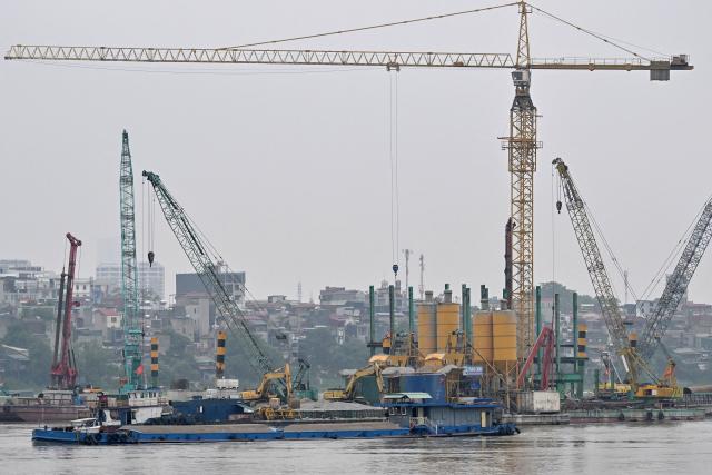 A barge carrying building materials passes the construction site of a bridge over the Red River in Hanoi on June 16, 2026. (Photo by Nhac NGUYEN / AFP)