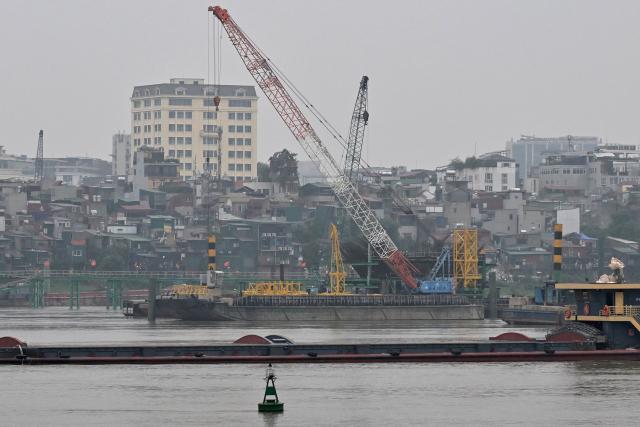 A barge carrying building materials passes the construction site of a bridge over the Red River in Hanoi on June 16, 2026. (Photo by Nhac NGUYEN / AFP)