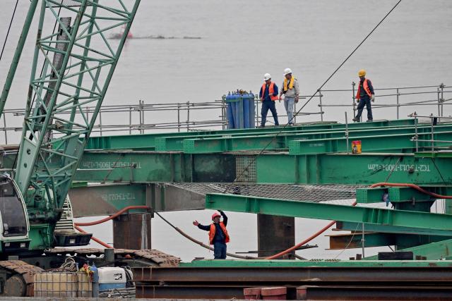 Workers use heavy construction equipment to build a new bridge over the Red River in Hanoi on June 16, 2026. (Photo by Nhac NGUYEN / AFP)