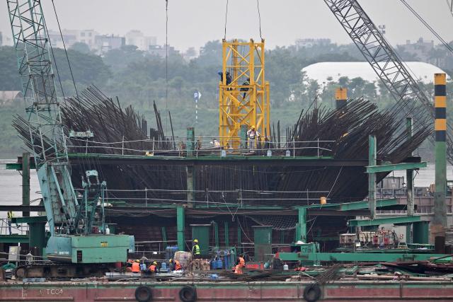 Workers use heavy construction equipment to build a new bridge over the Red River in Hanoi on June 16, 2026. (Photo by Nhac NGUYEN / AFP)