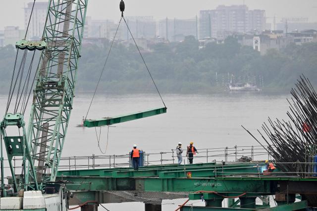 Workers use heavy construction equipment to build a new bridge over the Red River in Hanoi on June 16, 2026. (Photo by Nhac NGUYEN / AFP)