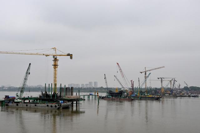 Workers use heavy construction equipment to build a new bridge over the Red River in Hanoi on June 16, 2026. (Photo by Nhac NGUYEN / AFP)