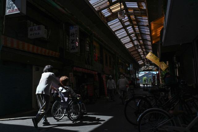 (FILES) This photo taken on October 1, 2025 shows an elderly woman (2nd L) being pushed through the Tsurumibashi "shotengai", an old covered shopping street in the Nishinari ward of Osaka. In Yo Kusakabe's taboo novel, a young doctor advocates chopping off elderly patients' useless limbs as a groundbreaking solution to super-ageing Japan's overstressed care industry. Now adapted into a film, "Haiyoshin (Useless Body)" has attracted huge controversy since its release last month in Japan, but has also focused attention on the struggling care sector in a country with the world's second-oldest population. (Photo by Richard A. Brooks / AFP)